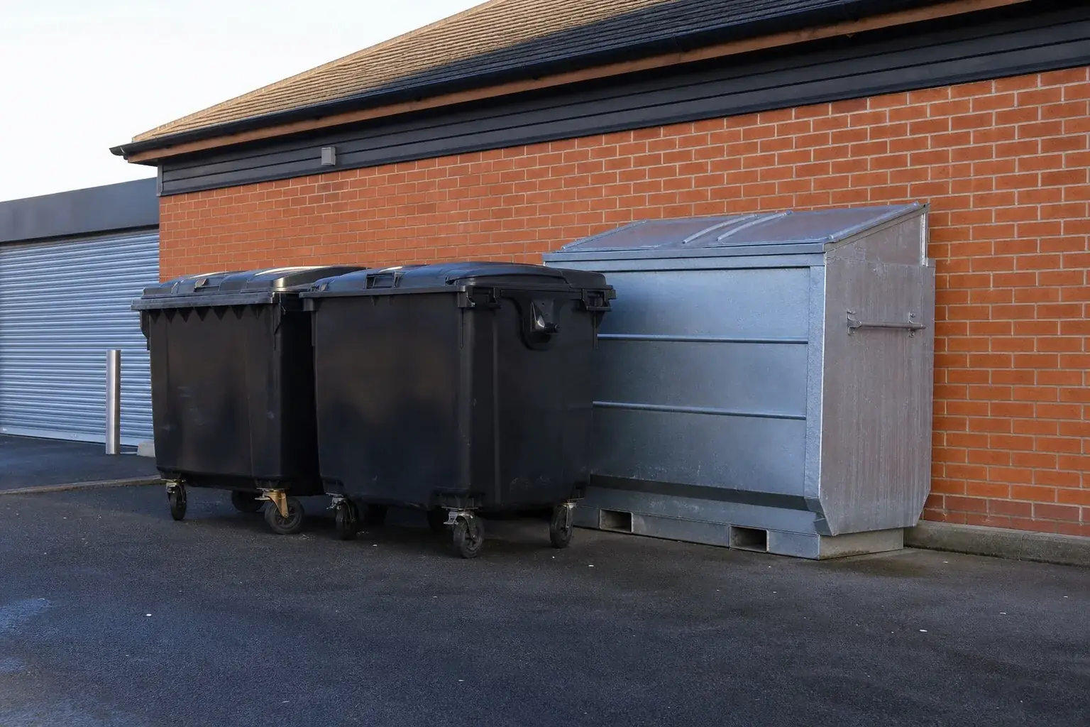 Commercial wheelie bins and a steel trade waste container in the service yard behind a retail parade