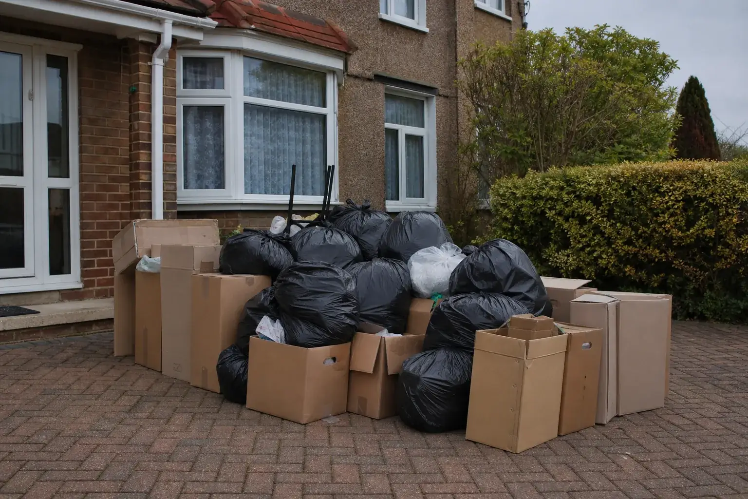 Bagged household rubbish and cardboard boxes stacked on a suburban driveway ready for collection